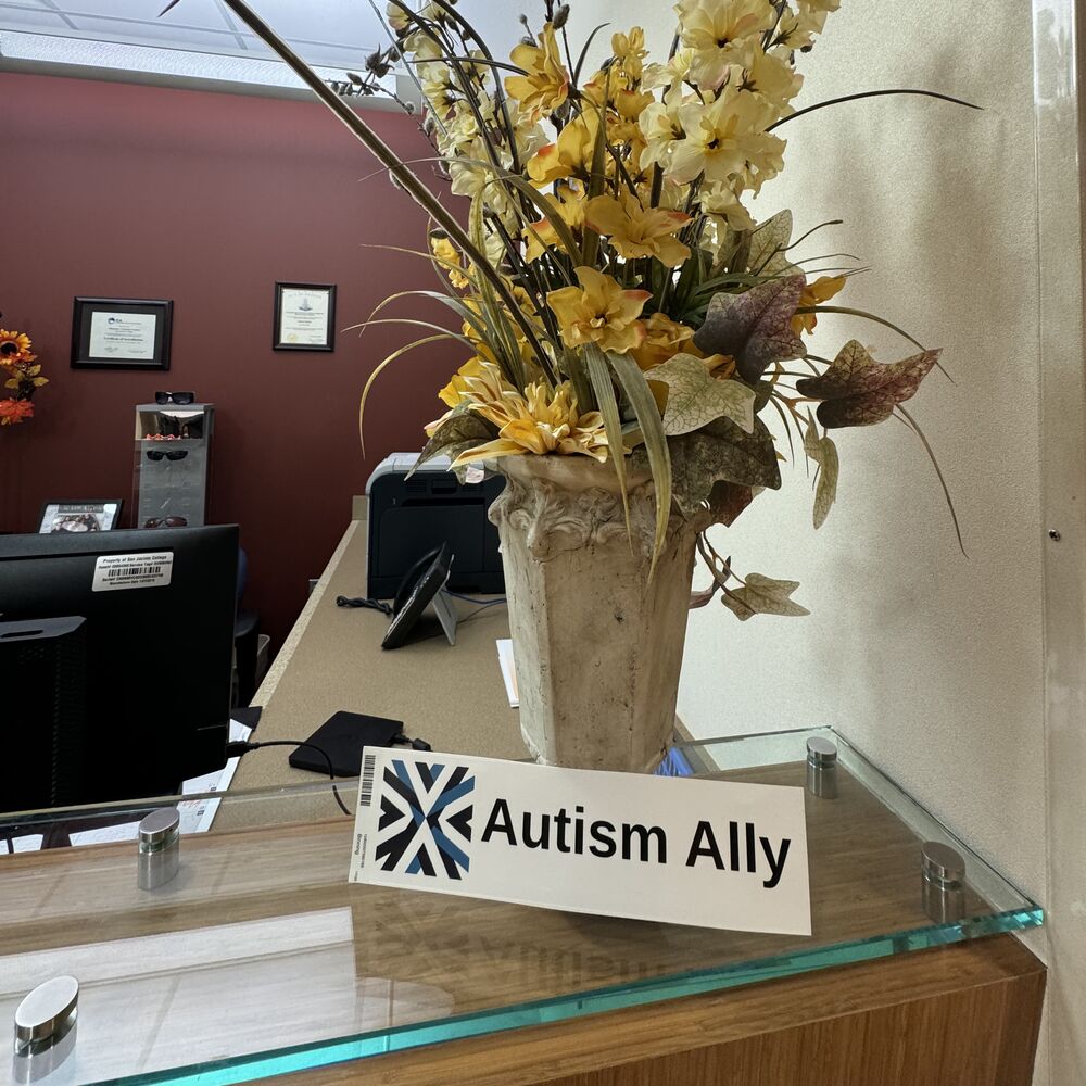 The Autism Ally sticker on a glass display case beside a flower arrangement.