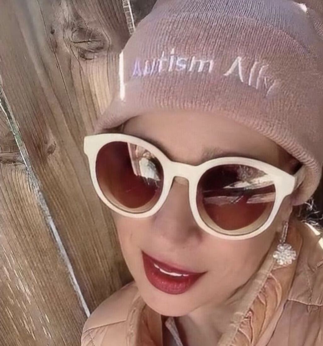 A woman in a pink Autism Ally beanie beside a wooden fence.