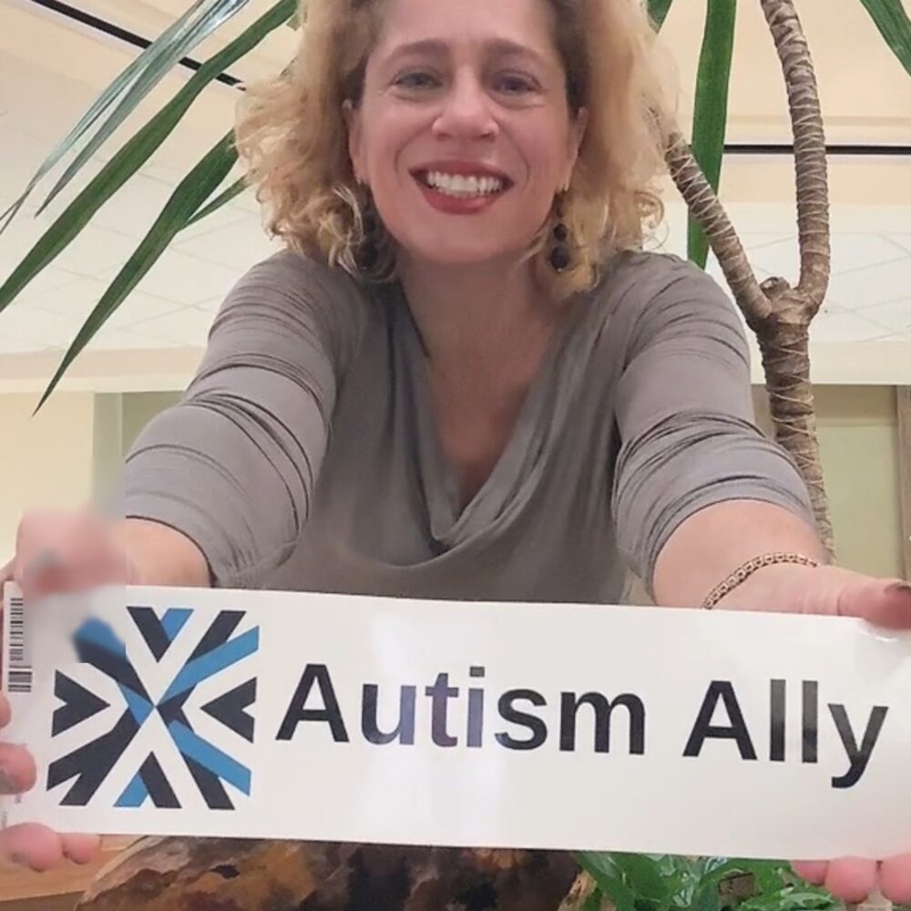 A woman holding the long Autism Ally sticker toward the camera.