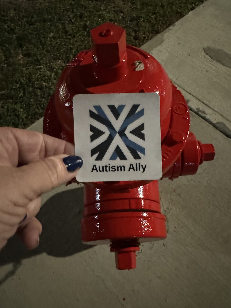 A hand holding the Autism Ally sticker against a fire hydrant at night.